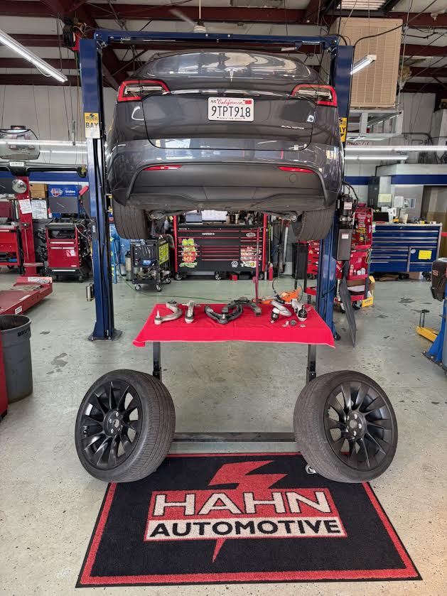 Tesla Model Y on the lift at Hahn Automotive with suspension components laid out on the Hahn shop mat